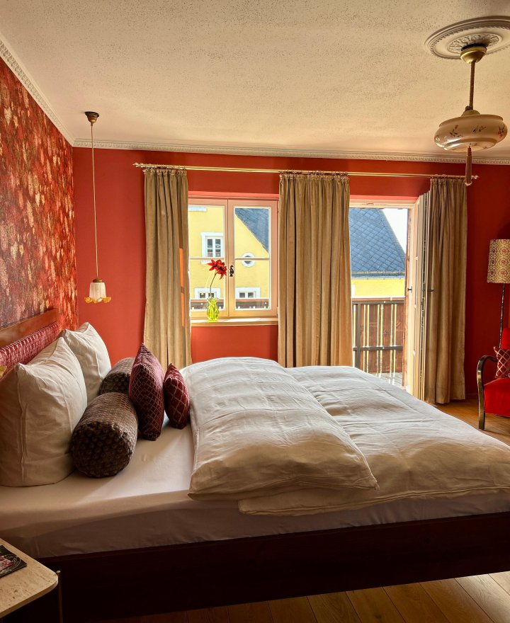 Hotelkamer met raam, gordijnen en een warme rode wand met bloemen op de vensterbank, door cestsjoukje