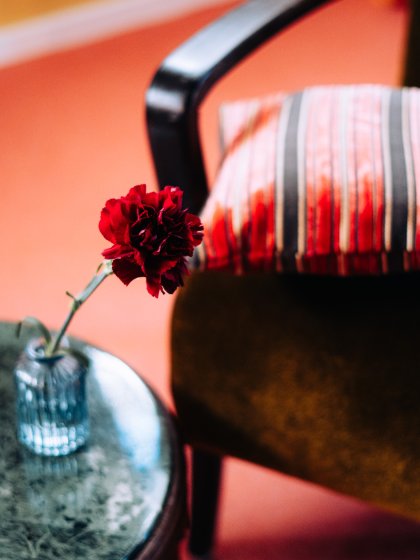 Hotelkamer met vintage fauteuil en een rode anjer als kleuraccent, door cestsjoukje