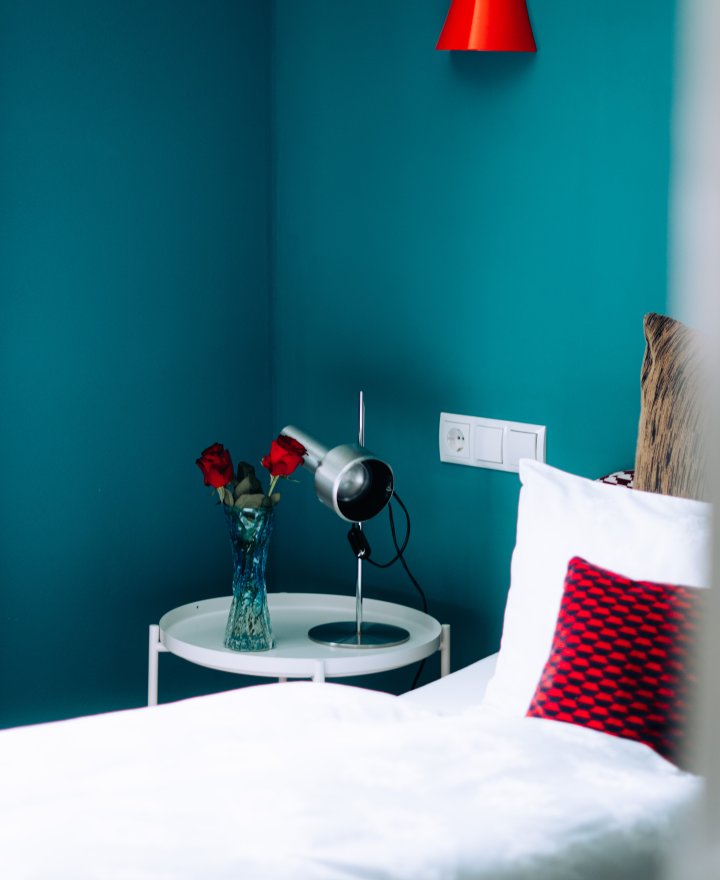 Hotelkamer met petrolblauwe wand en een rode hanglamp, door cestsjoukje