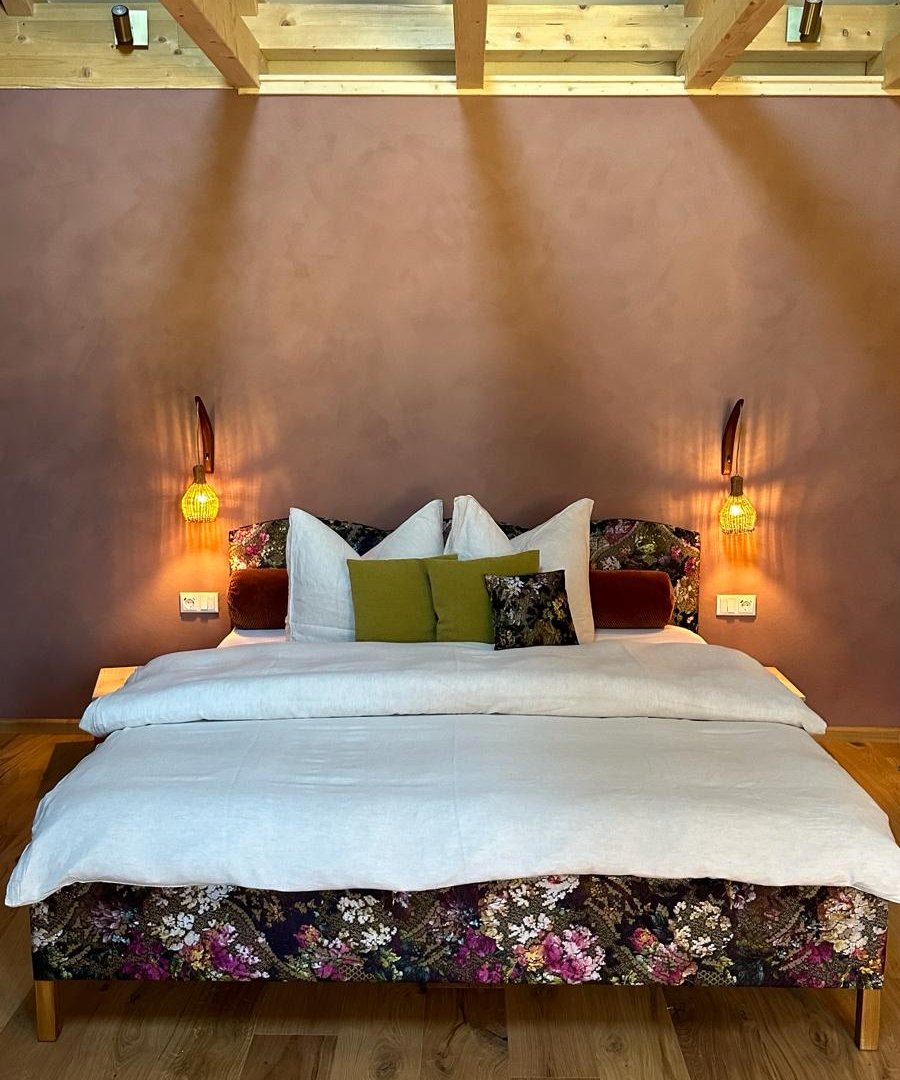 Hotelkamer met bloementextiel op het bed, warme wandlampjes en houten balkenplafond, door cestsjoukje