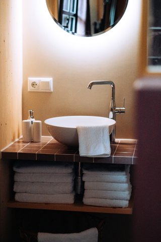 Hotelbadkamer met waskom op betegeld wastafelmeubel met ronde spiegel, messing kraan en opgerolde handdoeken, cestsjoukje